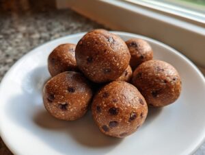 A small pile of homemade, round protein balls studded with mini chocolate chips, resting on a white plate.