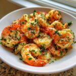 A white bowl filled with perfectly cooked, juicy air fryer shrimp seasoned with garlic and fresh parsley.