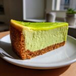 A vibrant slice of key lime cheesecake featuring a thick graham cracker crust and bright green lime topping.