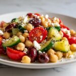 Close-up of a vibrant mediterranean chickpea salad featuring chickpeas, cherry tomatoes, cucumber, olives, and crumbled feta cheese.