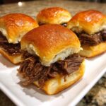 Four glistening Mississippi pot roast sliders piled high with shredded beef and melted cheese on soft buns.