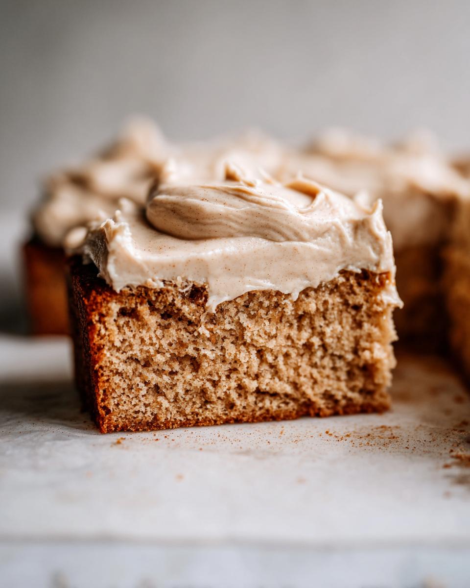 Close-up of a moist slice of applesauce cake topped with thick, swirled cinnamon frosting.