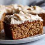Close-up of a thick slice of moist applesauce cake topped with creamy, spiced frosting.