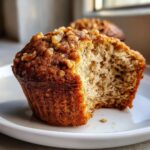 Close-up of a banana nut muffin with a bite taken out, showing the moist crumb and walnut topping.