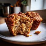 Close-up of a moist honey bran muffin with a bite taken out, showing the crumb texture next to a whole muffin.
