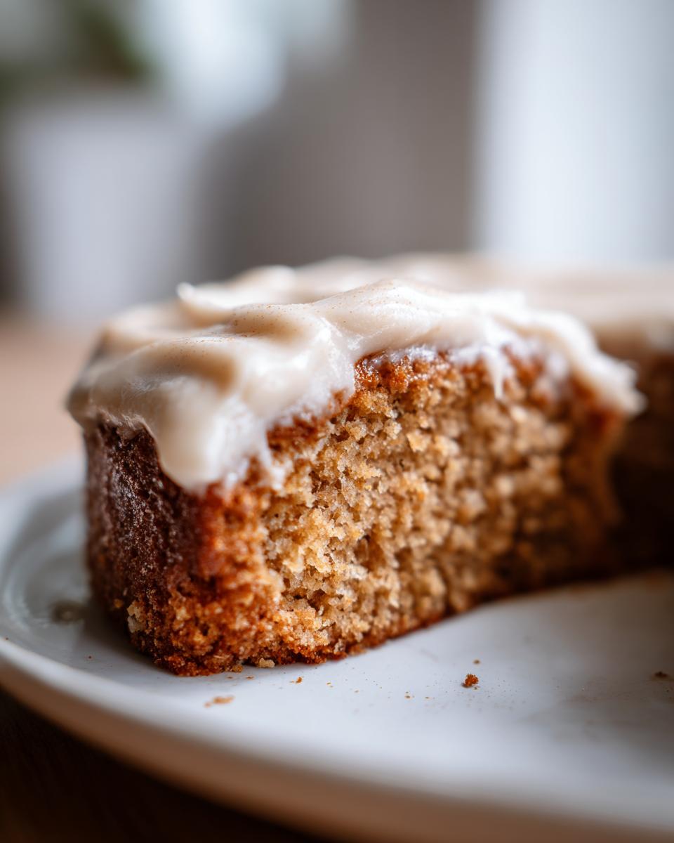 Close-up of a moist slice of applesauce cake showing the crumb texture and thick, creamy frosting.