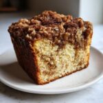 A close-up of a thick slice of sour cream coffee cake showing moist crumb and thick cinnamon streusel topping.