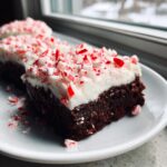 A rich, dark chocolate peppermint brownie slice topped with thick white frosting and crushed candy canes.