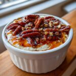 Close-up of a creamy pecan pie dip topped generously with glazed pecans and caramel sauce in a white ramekin.