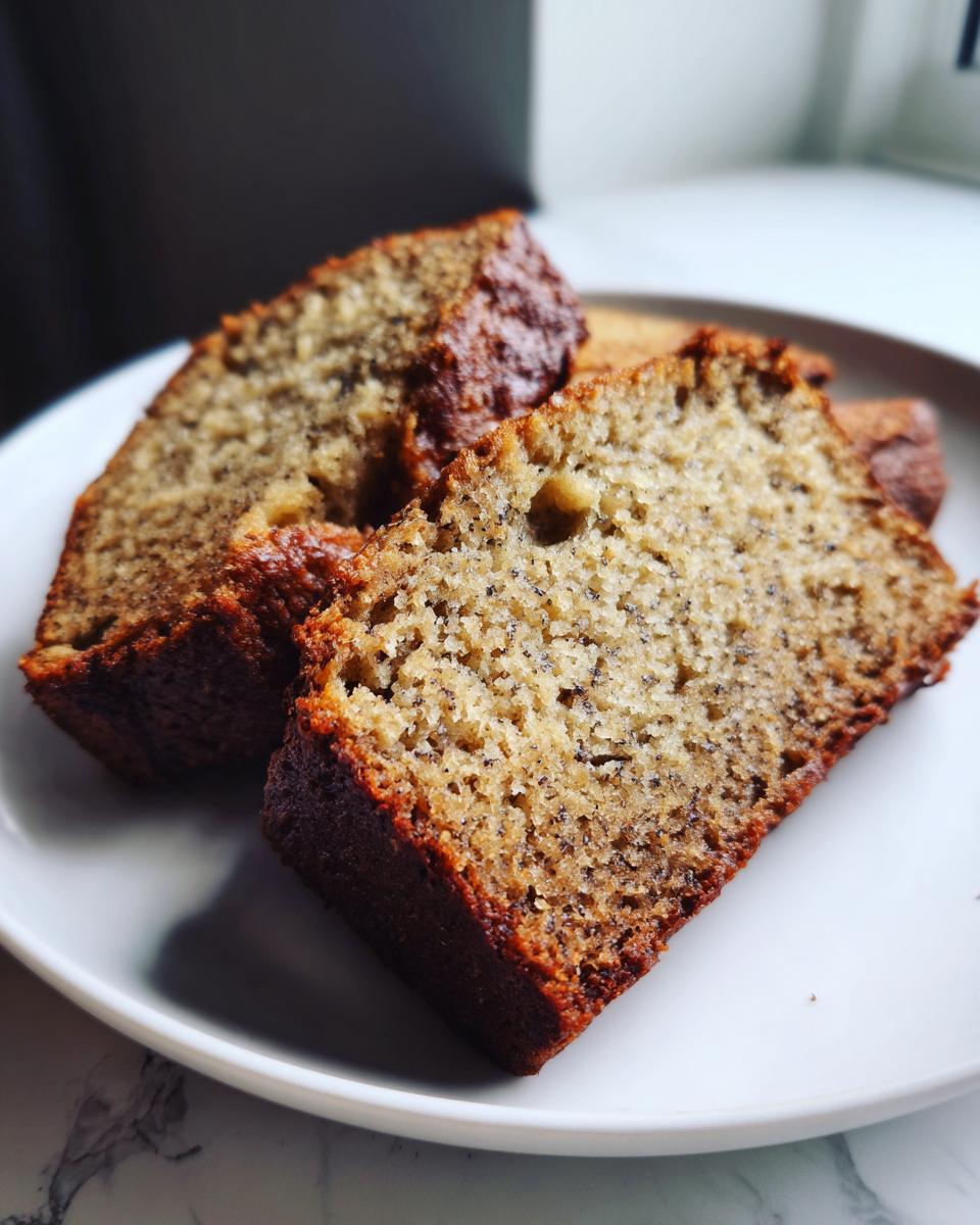 Close-up of two thick slices of moist Protein banana bread with a dark, caramelized crust on a white plate.
