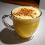 A close-up of rich, yellow homemade eggnog topped with foam and sprinkled with cinnamon.