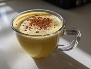 Close-up of a glass mug filled with rich, yellow homemade eggnog, topped with foam and sprinkled with cinnamon.