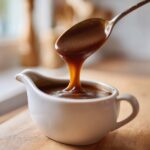 A spoonful of rich, thick turkey gravy is dripping back into a white ceramic gravy boat.