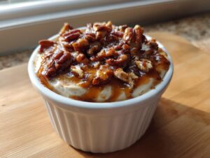 A close-up of a single serving of creamy pecan pie dip topped generously with gooey caramel sauce and chopped pecans.