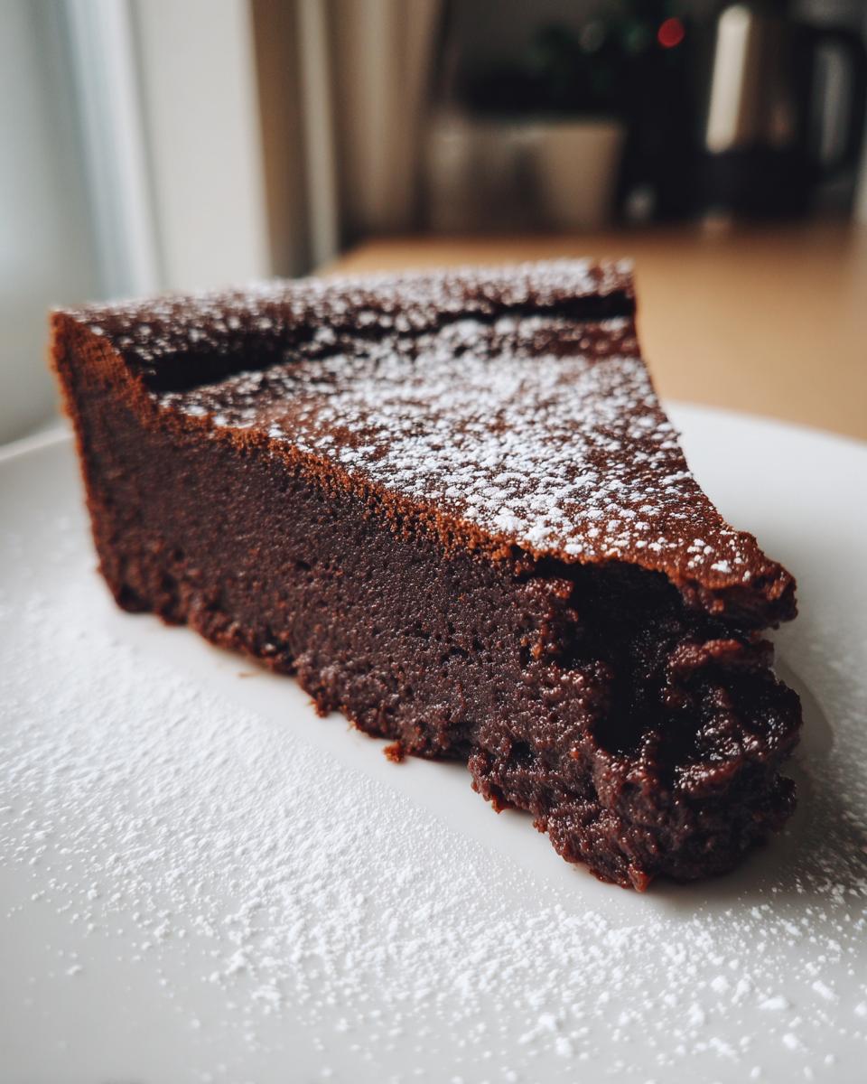 A decadent slice of flourless chocolate torte dusted generously with powdered sugar on a white plate.