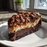 A thick slice of german chocolate cheesecake showing chocolate crust, creamy filling, and pecan coconut topping.