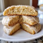 Stack of soft eggnog cookies, one cut in half to show the moist interior and topped with a white glaze and nutmeg.
