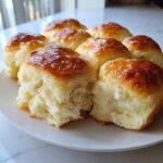 A cluster of freshly baked, golden-brown sourdough discard rolls pulled apart on a white plate.