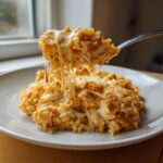 A fork lifts a bite of creamy, cheesy chicken and rice, showing long, gooey cheese pulls.