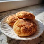 Three soft, chewy Snickerdoodle cookies coated in cinnamon sugar resting on a white plate.