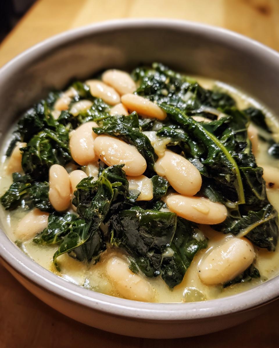 A close-up view of creamy tuscan white bean soup featuring plump white beans and dark green kale in a light broth.