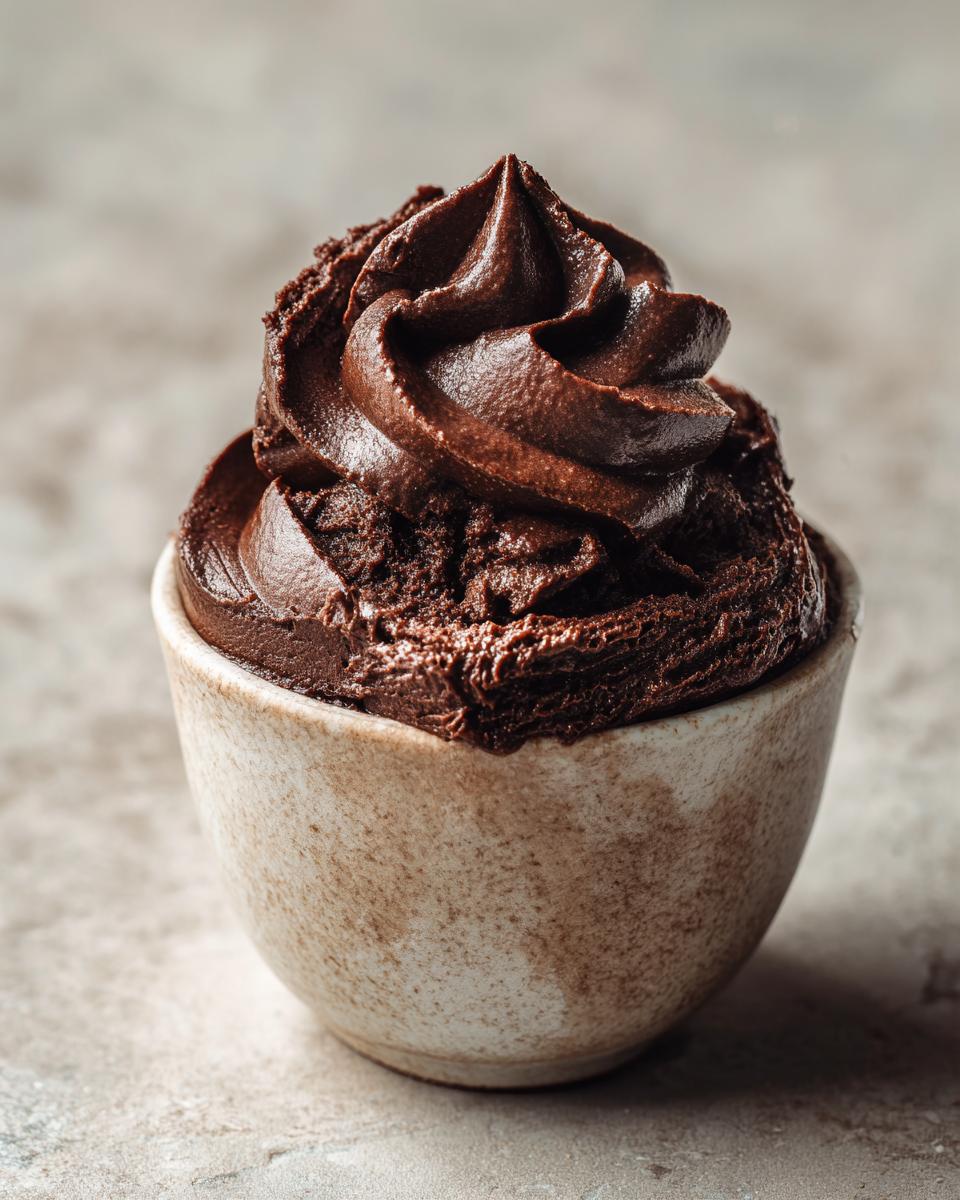 A close-up of rich, dark chocolate mousse piped into a small, speckled ceramic cup.