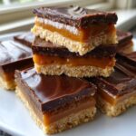 Close-up of stacked homemade Twix bites showing a shortbread base, thick caramel layer, and glossy chocolate topping.