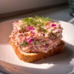A generous scoop of creamy salmon salad with red onion and dill served on a slice of toasted bread.