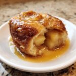 A warm, baked apple dumpling cut open to show soft apple filling, drizzled with rich caramel sauce.