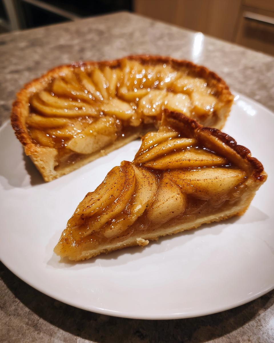 A slice of amazing apple tart, featuring thinly sliced, glazed apples sprinkled with cinnamon, next to the rest of the apple tart.