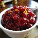 Close-up of homemade cranberry sauce in a white bowl, topped with bright orange zest.