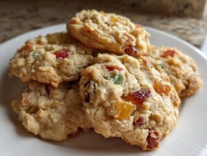 A stack of freshly baked fruitcake cookies featuring colorful candied fruit pieces on a white plate.