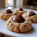 A close-up of four sugar-coated kiss cookies topped with a swirl of chocolate filling.