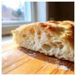 Close-up of the airy, open crumb structure of freshly baked pizza dough on a wooden board.