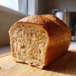 Close-up of a freshly baked, soft loaf of whole wheat bread sliced open on a wooden cutting board.