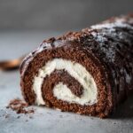 A close-up cross-section of a rich chocolate yule log cake showing the dark sponge rolled with white cream filling.