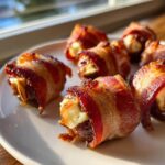 Close-up of several crispy, bacon-wrapped stuffed dates arranged on a white plate, glistening in the sunlight.