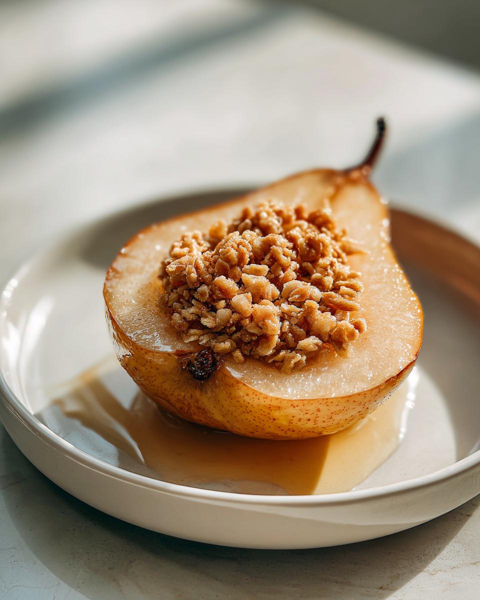 A single baked pear half, filled with a crunchy oat crumble topping, sitting in syrup on a white dish.