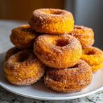 A tempting stack of freshly baked pumpkin donuts coated generously in cinnamon sugar.