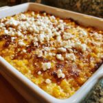 Close-up of hot, baked street corn dip in a white casserole dish, topped with crumbled white cheese.