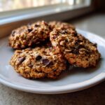 Four freshly baked banana oatmeal cookies loaded with visible oats and chocolate chips, resting on a light blue plate.