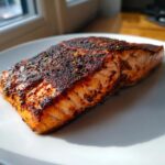 Close-up of a thick, perfectly cooked blackened salmon fillet with a dark spice crust on a white plate.