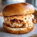 Close-up of a juicy patty on a toasted bun generously topped with creamy orange burger sauce.