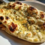 Close-up, appetizing shot of freshly made naan bread brushed with melted butter and sprinkled with green herbs.