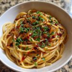 Close-up of spaghetti tossed in sauce, topped with rich caramelized onion pasta and fresh parsley.