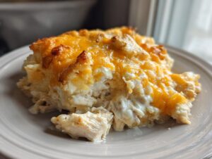 A close-up serving of creamy chicken and rice casserole topped with melted, browned cheddar cheese.