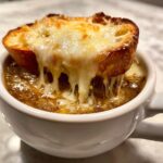 Close-up of rich french onion soup topped with a crouton covered in melting, stringy cheese.