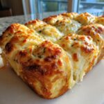 Close-up of baked Hawaiian roll garlic bread topped with melted, browned cheese and herbs.
