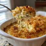 A spoonful of hot, cheesy popper dip, showing long cheese pulls, lifted from a baked casserole dish.