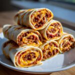 A stack of freshly cut taco pinwheels filled with seasoned ground beef and melted cheese, ready to eat.
